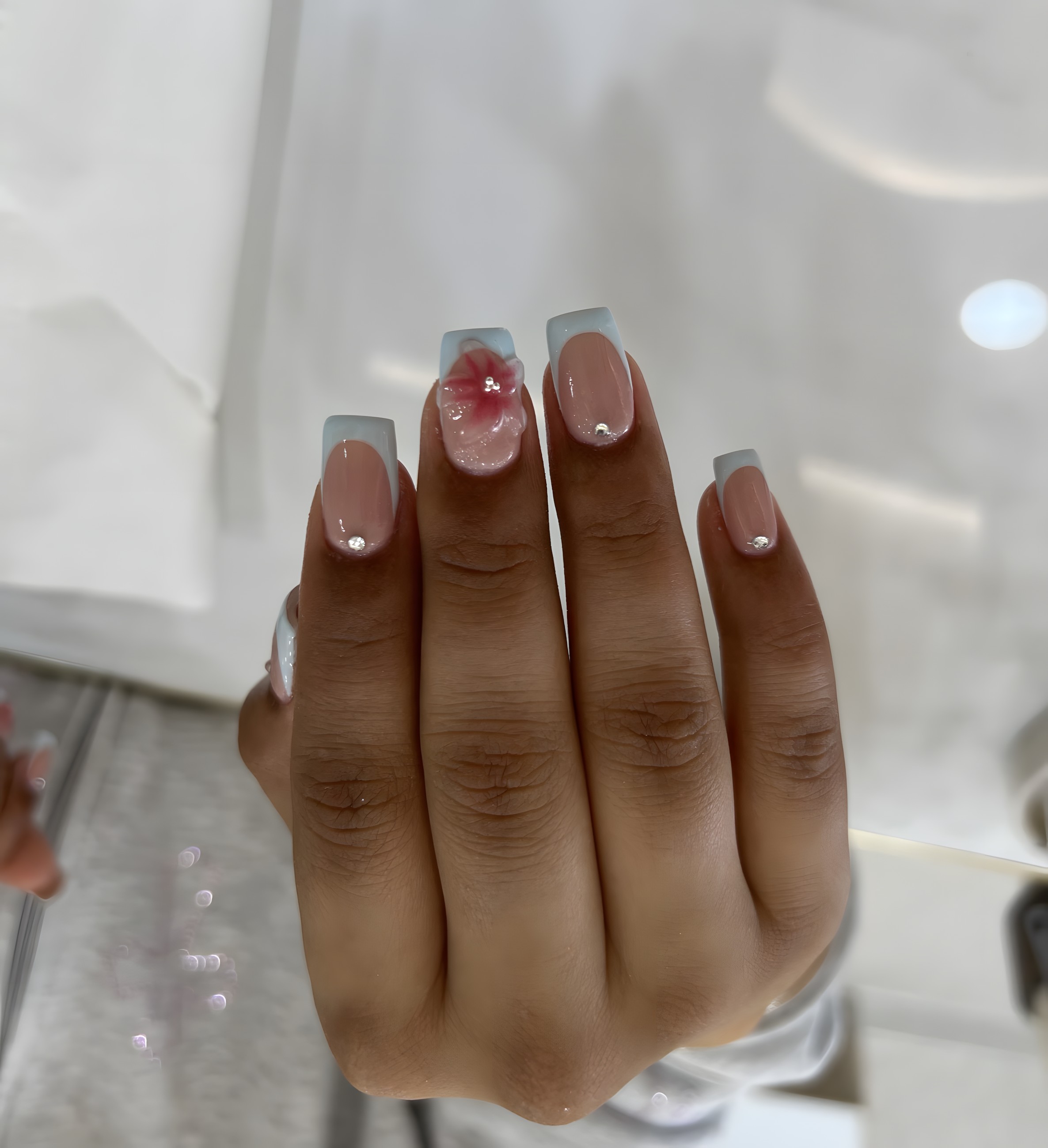 Pale blue French tip nails with a hand-painted pink floral accent