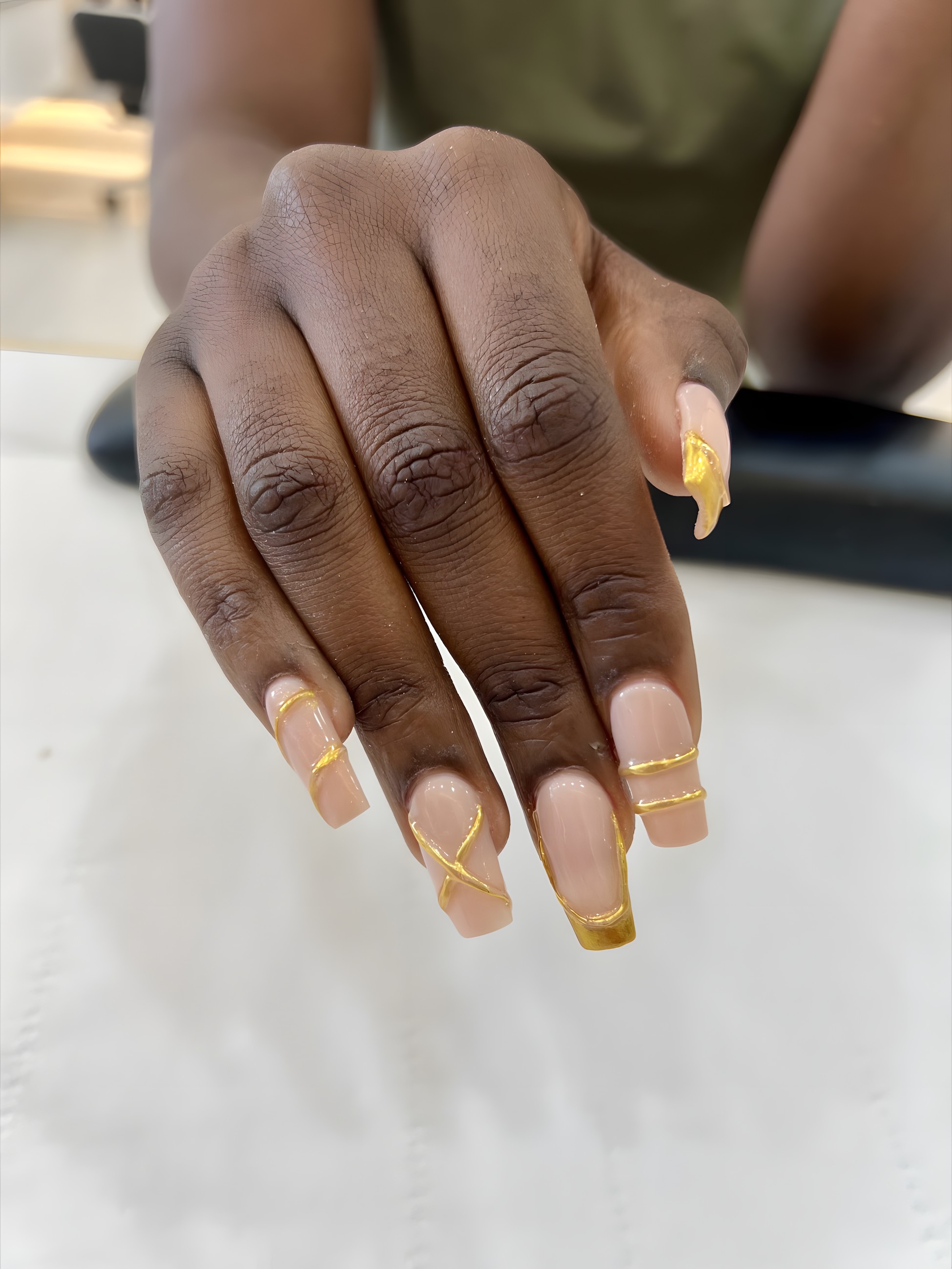 Nude square nails with a hand-painted gold outline and crossover detail